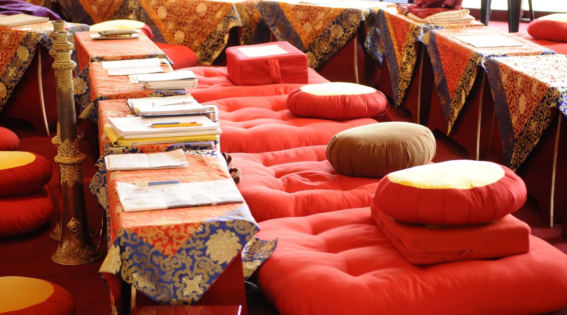 Shédra — Études bouddhistes à Karma Ling Maison de la Sagesse pour étude du Shédra à Karma Ling — coussins de méditation rouges et tables basses ornées de brocarts tibétains