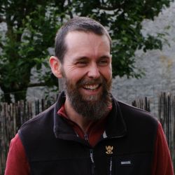Portrait de Lama Kada, enseignant bouddhiste, souriant, en veste sombre, en extérieur