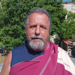 Portrait de Lama Mingyur, enseignant bouddhiste, en châle bordeaux, en extérieur devant un arbre