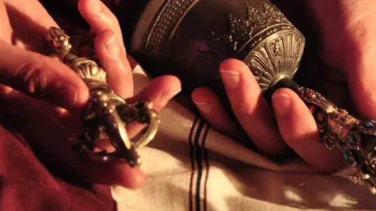 Mains d'un retraitant tenant le vajra et la cloche rituelle, posés sur un châle de méditation blanc et un zen monastique rouge