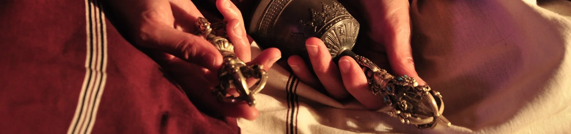 Mains d'un retraitant tenant le vajra et la cloche rituelle, posés sur un châle de méditation blanc et un zen monastique rouge